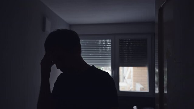 Silhouette of depressed sad man in dark room with window shutters pulled down