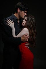 A passionate kiss between a man in a black suit and a woman in a red dress on a dark background.
