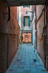 Fototapeta na wymiar Lonely path way along the Venetian city with high facades and mystic shadows