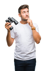 Young handsome man looking through binoculars over isolated background serious face thinking about...