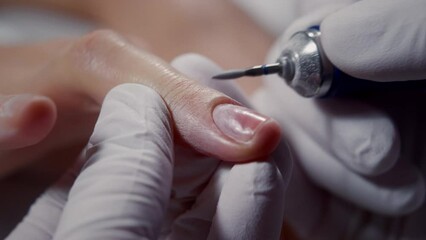 Master peels gentle skin around woman nail with electric polisher in manicure salon closeup. Beautician removes dry skin and cuticle from nail with drill in shop. Professional manicurist service - Powered by Adobe