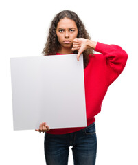 Young hispanic woman holding blank banner with angry face, negative sign showing dislike with thumbs down, rejection concept