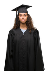 Young hispanic woman wearing graduation uniform with a confident expression on smart face thinking serious