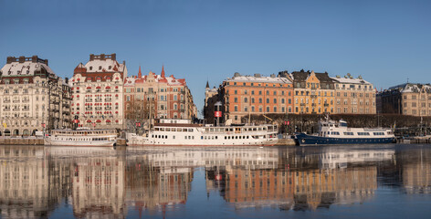 Fototapeta na wymiar Hotel, steam commuter ferries and boats at the pier Strandvägen at the icy bay Nybroviken a part of the Ladugårdslandsviken a sunny winter day in Stockholm