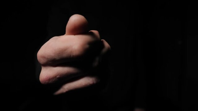 Stranger makes a gesture of money with fingers on a black background. Close-up of a man's hands gesturing to suggest a bribe. The man demands payment and returns the debt.