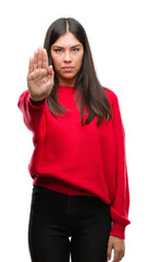 Young beautiful hispanic wearing red sweater doing stop sing with palm of the hand. Warning expression with negative and serious gesture on the face.