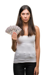 Young hispanic woman holding dollars with a confident expression on smart face thinking serious