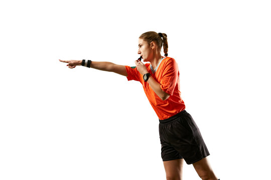Young woman, football referee in uniform pointing and blowing whistle, controlling game rules against white studio background. Concept of sport, competition, match, profession, coach