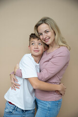 cool young teenager boy with white t-shirt posing together with his beautiful mother in front of brown background