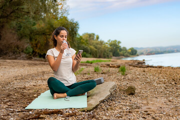 Naklejka na ściany i meble Taking a break, she hydrates with a sip from a glass bottle while sitting on her workout mat.