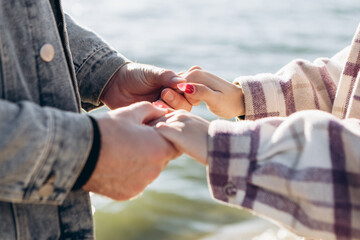 Cropped image hands young loving couple standing outside beach shore in sunny weather, hugging...