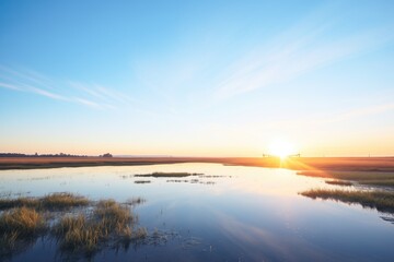 sunrise over a still marsh with a clear blue sky reflection