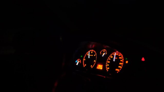 Orange light of the speedometer in the car. The car goes at a speed of one hundred and thirty kilometers per hour. The fuel gauge shows the full tank. A trip at night in the car.
