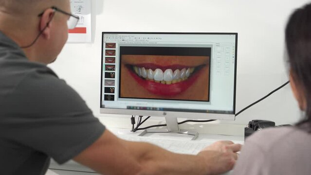 Cosmetic dentist shows photo of teeth smile to female patient on screen in modern dental clinic. Stomatologist, patient discuss modeling of veneers. Doctor explains photo of teeth to a woman.