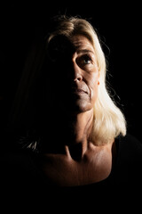 Older woman in her mid-fifties, blue eyes, blonde hair with leather jacket, head portraits isolated against a black background.