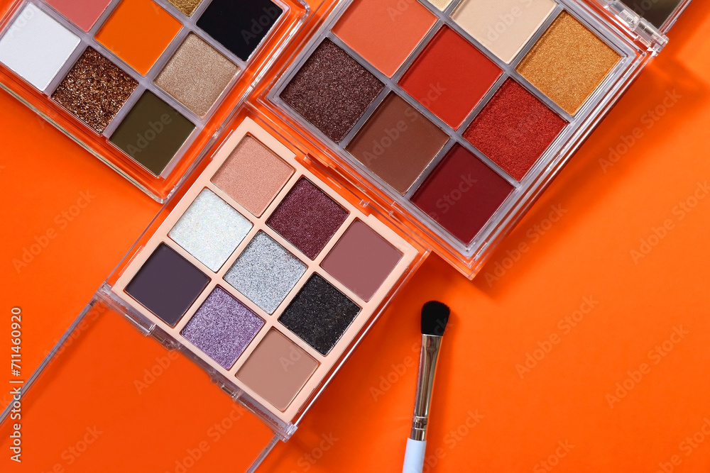 Wall mural colorful eyeshadow palettes and make up brush on orange background. top view.