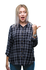 Young blonde woman over isolated background smiling with happy face looking and pointing to the side with thumb up.