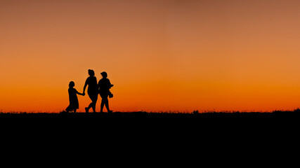 Fototapeta na wymiar Mother with daughters walking at sunset on the shore of the Ohio River