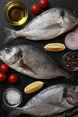 Fresh raw dorado fish, lemon wedges, spices and tomatoes on black table, flat lay