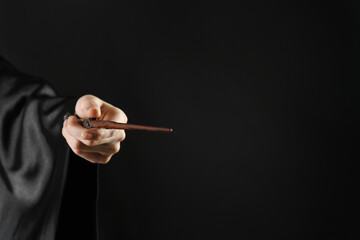Wizard holding magic wand on black background, closeup. Space for text