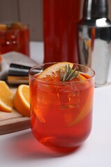 Aperol spritz cocktail, ice cubes, rosemary and orange slices in glass on white wooden table, closeup