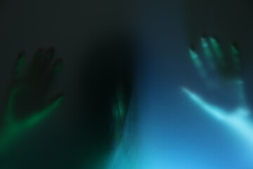 Silhouette of creepy ghost behind glass against color background