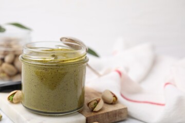 Tasty pistachio cream in jar and nuts on table, closeup. Space for text