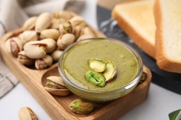 Tasty pistachio cream and nuts served on white table, closeup