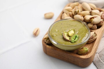 Tasty pistachio cream in bowl and nuts on white tiled table, closeup. Space for text