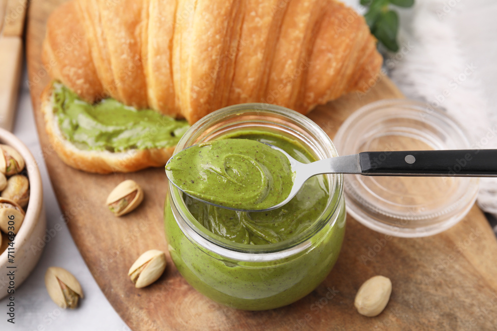 Poster tasty pistachio cream in jar, spoon and croissant on light table, closeup - Posters