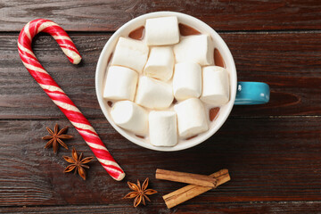 Tasty hot chocolate with marshmallows, candy cane and spices on wooden table, flat lay