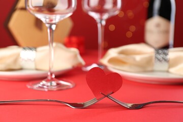 Joined forks with paper heart on red table, closeup. Romantic dinner
