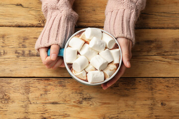 Woman with cup of tasty hot chocolate and marshmallows at wooden table, top view