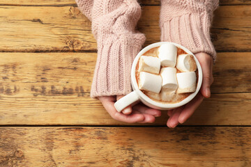 Woman with cup of tasty hot chocolate and marshmallows at wooden table, top view. Space for text