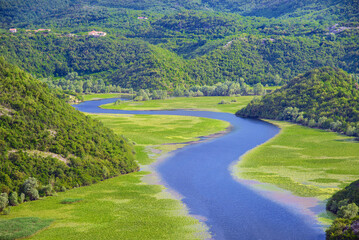 Meandering Rijeka Crnojevica river behind green mountains amd hills in Skadar Lake National Park, Montenegro, natural summer landscape background.