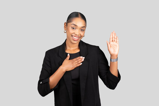 Radiant young woman in black business attire smilingly takes an oath with her right hand raised