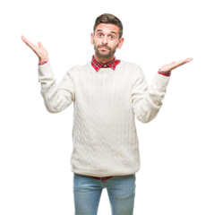 Fototapeta premium Young handsome man wearing winter sweater over isolated background clueless and confused expression with arms and hands raised. Doubt concept.