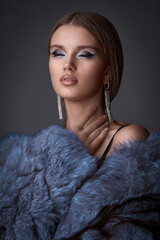 Portrait of a young girl with exquisite makeup in a blue fur coat