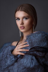 Portrait of a young girl with exquisite makeup in a blue fur coat