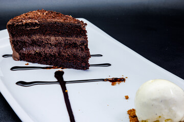 Chocolate cake on a white plate with ice cream on a black  background