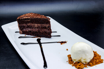 Chocolate cake on a white plate with ice cream on a black  background