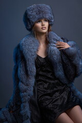A young girl with exquisite makeup in a blue fur coat, a hat and a short black dress.