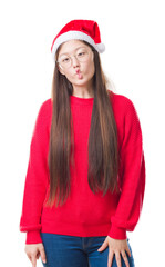 Young Chinese woman over isolated background wearing christmas hat making fish face with lips, crazy and comical gesture. Funny expression.