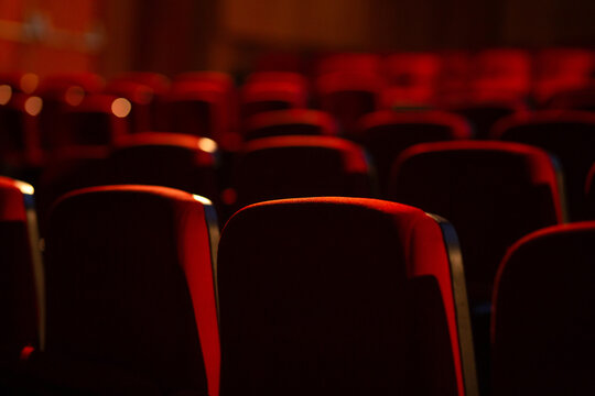 Detalhe de um teatro vazio. Várias fileiras de poltronas vermelhas fotografadas por trás. Fotografia com foco restrito.