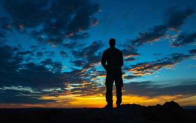 Silhouette of a man standing on top of a mountain and looking at the sunset