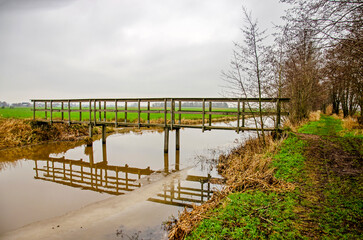 Montfoort, The Netherlands, January 13, 2024: wooden pedestrian bridge reflecting in a partially frozen canal in a nature reserve