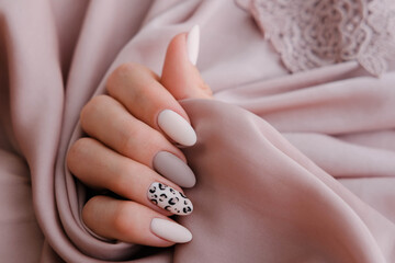 Woman's hand with a beautiful oval-shaped manicure. Autumn trend, beige color polishing with leopard pattern on nails with gel polish, shellac.
