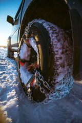 car with snow chains, bracelets. SUV wheel in snow, steel wheel. To overcome difficult road conditions, driving on ice. Weather situation. Selective focus. Vertical photo.