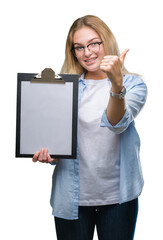 Young caucasian business woman holding clipboard over isolated background happy with big smile doing ok sign, thumb up with fingers, excellent sign