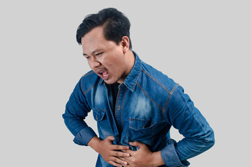 Young asian man having stomach ache or indigestion and pressing his stomach on isolated white...